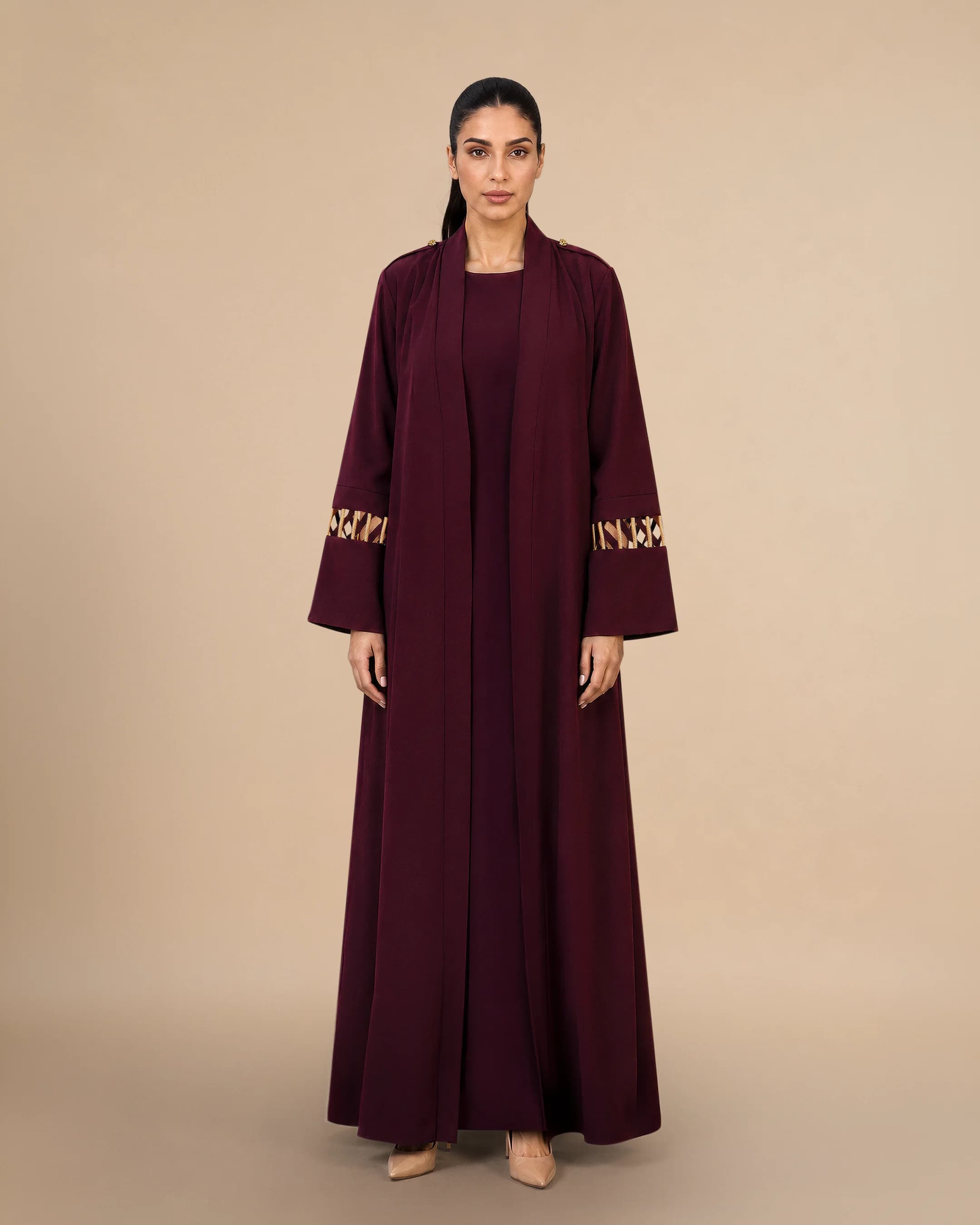 Bint Saeed Covent Garden Al Talli Abaya in Burgundy, front view. Luxury designer A-line abaya featuring UNESCO-recognised traditional Emirati Al Talli woven cuff trim, signature Knotted Line gold-tone shoulder epaulettes, and an elegant open-front silhouette. Buy Al Talli abaya UAE — heritage modest fashion and contemporary Emirati craftsmanship from Dubai and Abu Dhabi to the GCC and worldwide. Made in Abu Dhabi, United Arab Emirates. Worldwide shipping. Bint Saeed Abu Dhabi, United Arab Emirates.