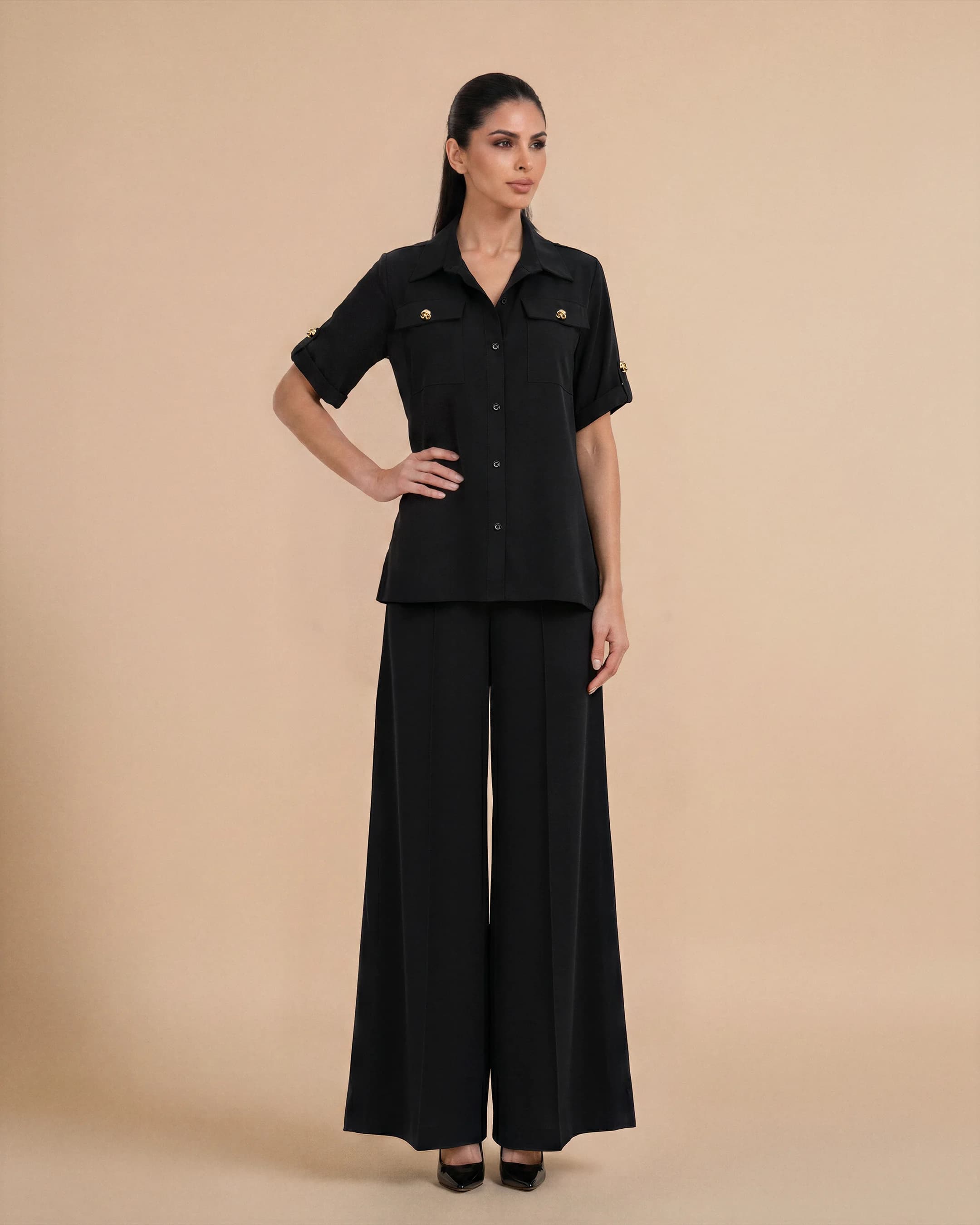 Bint Saeed Hyde Park Set in Deep Black, front view. Luxury designer travel set featuring an oversized premium crepe shirt and flowing wide-leg palazzo trousers with signature gold-tone Knotted Line buttons, functional chest pockets, and hidden side seam pockets. Buy understated elegance travel outfit UAE — modest khaleeji fashion and contemporary Emirati ready-to-wear from Abu Dhabi to London, Portofino, Rabat, Singapore, Miami, Los Angeles, Brunei, and worldwide. Made in Abu Dhabi, United Arab Emirates. Worldwide shipping. Bint Saeed Abu Dhabi, United Arab Emirates.
