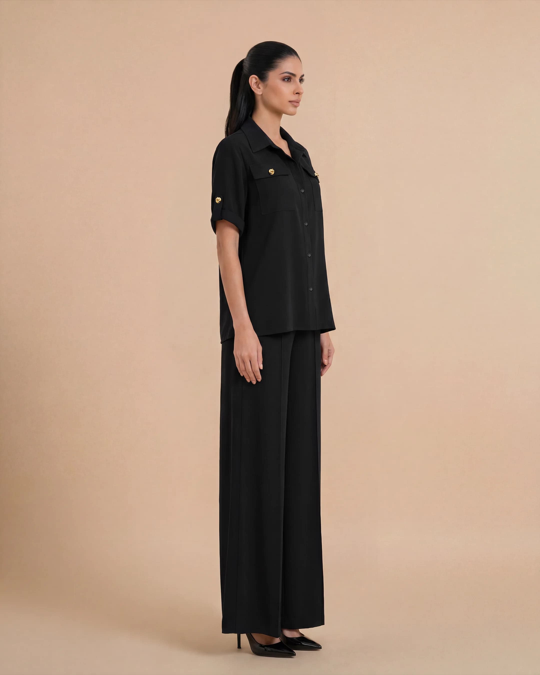 Three-quarter view of the Bint Saeed Hyde Park Set in Deep Black showcasing fluid premium crepe drape, oversized shirt silhouette, flowing palazzo movement, and signature Knotted Line buttons. Luxury Emirati coordinate travel set — premium shirt and palazzo pairing for women in Abu Dhabi, London, Portofino, Rabat, Singapore, Miami, Los Angeles, Brunei, and international wardrobes. Made in Abu Dhabi, United Arab Emirates. Worldwide shipping. Bint Saeed Abu Dhabi, United Arab Emirates.